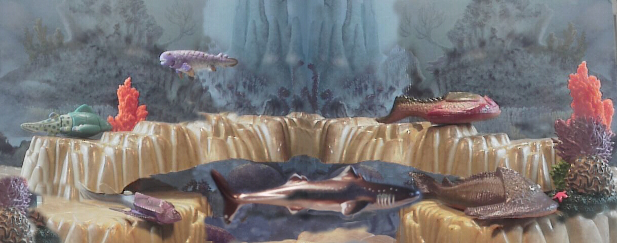 Prehistoric fish are relatively rare. The Starlux company in France produced the Drepanaspis and Hemicyclaspis on the right, and in the upper left by Cadbury Yowie from Australia are the Groenlandaspis and Ducabrook Rhizodont. Center from Japan is the Kaiyodo Dino Tales shark Cladoselachdae, and lower down is Bothriolepis.